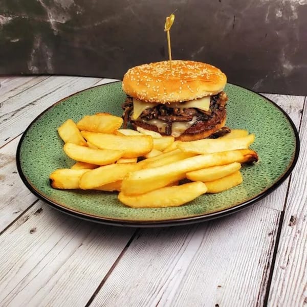 Mushroom Swiss burger with a sesame seed bun and a side of golden french fries on a green plate.
