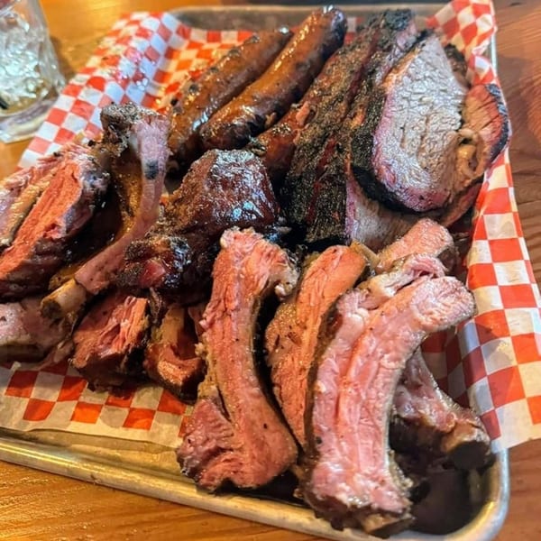 A metal tray filled with various cuts of barbecue meat, including ribs, brisket, and sausages.