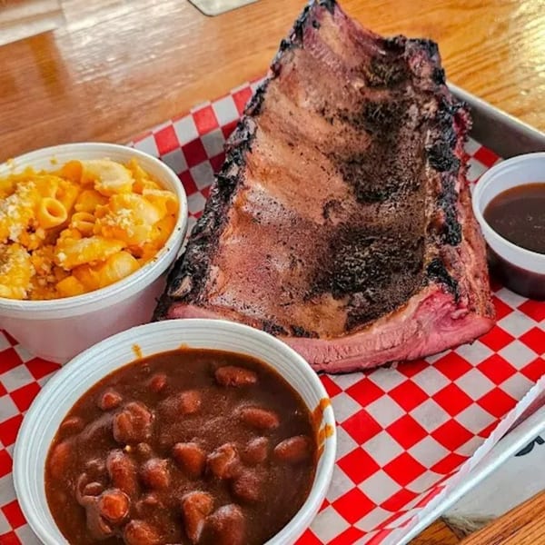 Smoked ribs, macaroni and cheese, and baked beans on a red and white checkered tray.